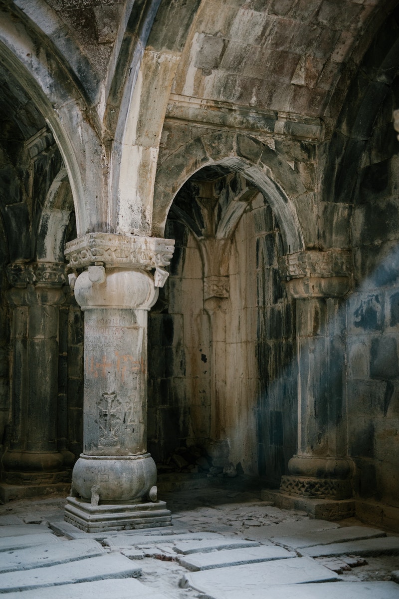 Interior of ancient stone masonry palace with arched passages and ornamental columns on shabby cement floor with ray of light